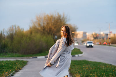 Beautiful smiling girl with long hair in a grey trench coat outdoors on the street spring