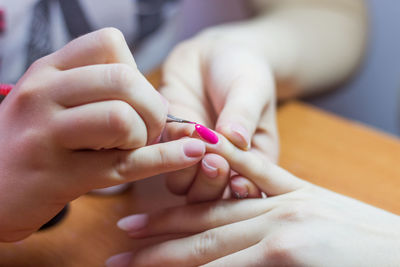 Cropped hands of woman painting friend fingernail at home