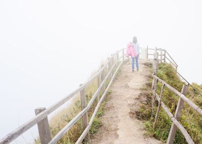 Man walking on railing against clear sky