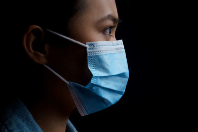 Close-up of young woman wearing flu mask standing against black background