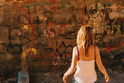 Rear view of woman standing against graffiti wall on sunny day