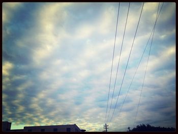 Low angle view of power lines against cloudy sky