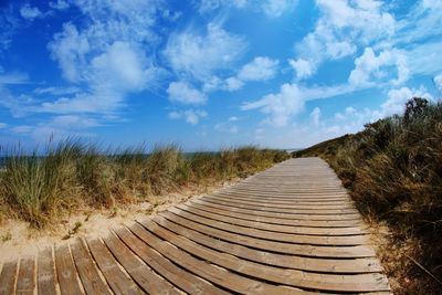 Surface level of boardwalk on landscape against sky