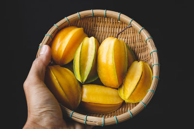 Close-up of hand holding orange fruit against black background