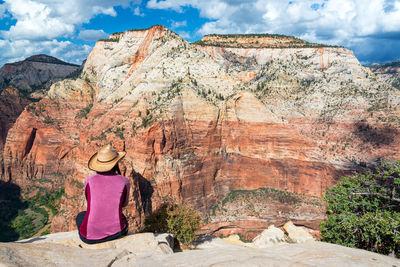 Woman sitting on rock against cloudy sky