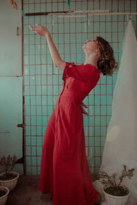 Young woman in red dress gesturing while standing at home