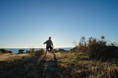 Man walking on field against clear blue sky