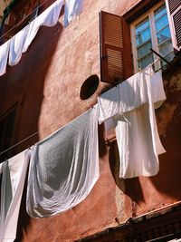White sheets and clothes hanging and drying against a colorful facade with sunlight and shadows 