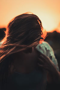 Side view of young woman against orange sky