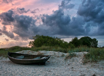 Boat moored on shore against sky during sunset