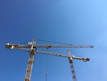 Low angle view of crane against clear blue sky