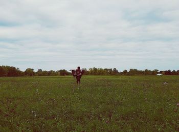 Rear view of man standing on grassy field against cloudy sky