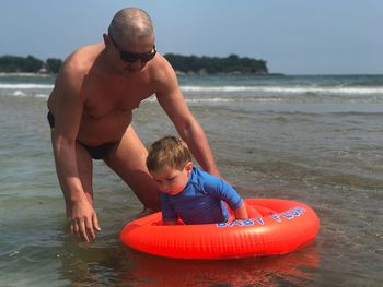 Father and son on beach against sky