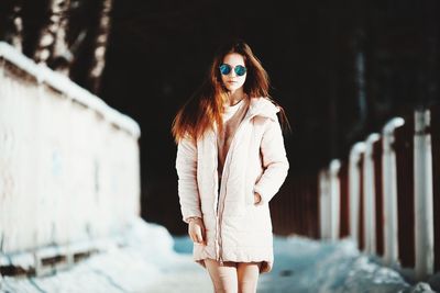 Portrait of young woman in warm clothing standing on footpath during winter