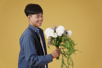 Young man holding flower while standing against yellow background