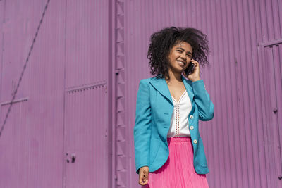 Full length of young woman using phone while standing against pink wall