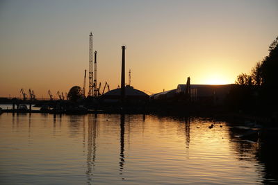 Silhouette cranes by lake against clear sky during sunset