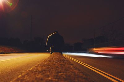 Silhouette man on illuminated road against sky at night