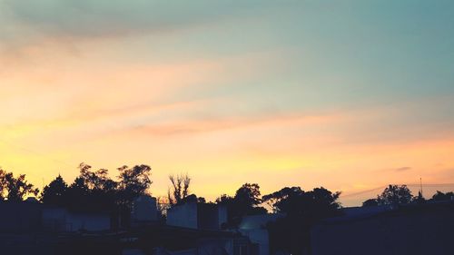 Silhouette houses and trees against sky during sunset