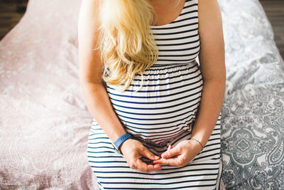 Midsection of pregnant woman sitting on bed