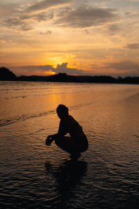 Silhouette man standing in sea against sky during sunset