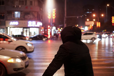 Rear view of man standing on city street at night