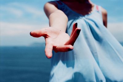 Midsection of woman gesturing while standing against sea