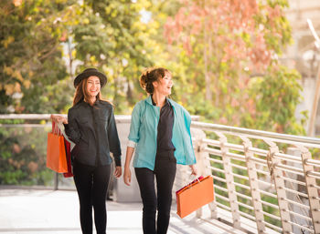 Happy friends with shopping bags walking on elevated walkway