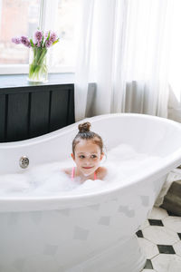 Happy little girl having fun in bath with foam at home