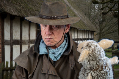 Senior man wearing hat looking at sheep toy at farm