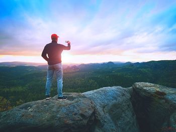 Amateur takes photos with smart phone on peak of rock. foggy landscape, spring sunrise in valley 