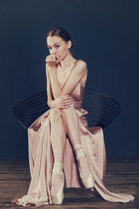 Portrait of a ballerina in a pink dress is sitting on a chair with her leg in the slit of the dress