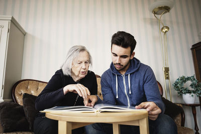 Caretaker and senior woman discussing while reading book at nursing home