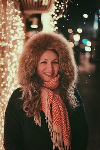 Portrait of happy woman standing against illuminated lights at night