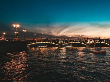 Illuminated bridge over sea against sky in city at night