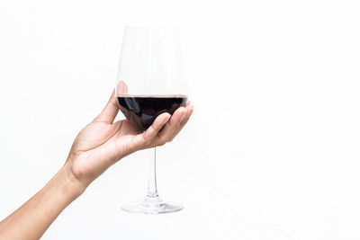 Close-up of hand holding wine glass against white background