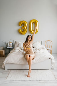 Happy woman holds a birthday cake with a candle in her hands, sitting on the bed in the bedroom