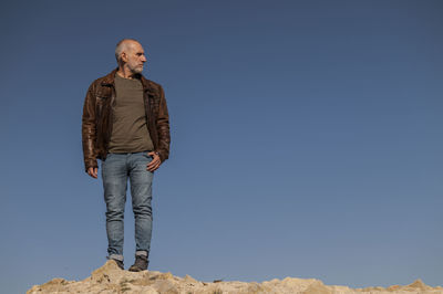 Full length of adult man with brown leather jacket against blue clear sky