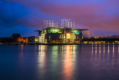 Illuminated buildings by river against sky at night