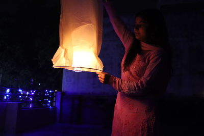 Woman standing by illuminated lamp at night