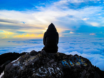 Rear view of man sitting on rock against sky