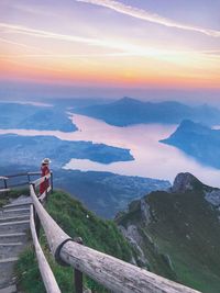 Man standing on railing by mountain against sky