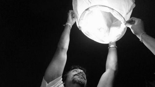 Close-up low angle view of man releasing paper lantern against clear sky at night