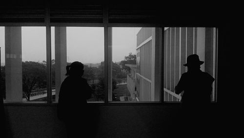 Rear view of silhouette two womans in physical distance standing by window
