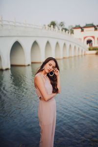 Young woman standing against bridge over water