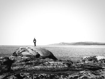 Man standing on rock formation by sea against clear sky