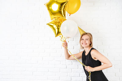 Young woman holding balloons against wall