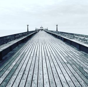 Wooden footbridge on pier against sky