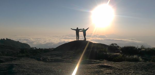 Silhouette men standing on mountain peak against sky during sunset