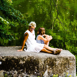 Rear view of women sitting by lake against trees